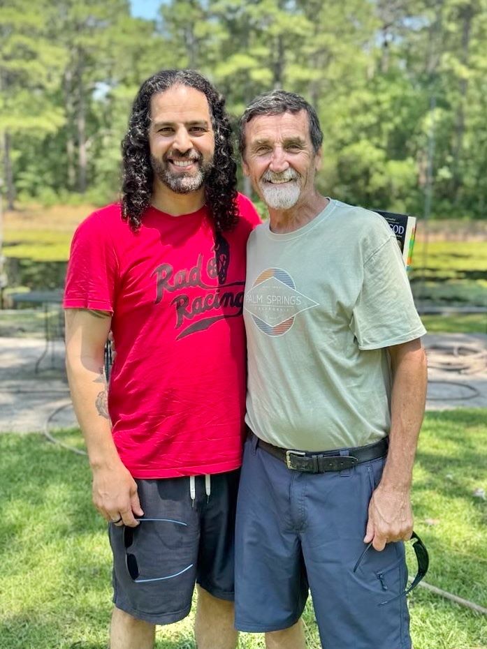 Glenn Sorrentino and Chris Bledsoe smiling together outdoors beside a pond.